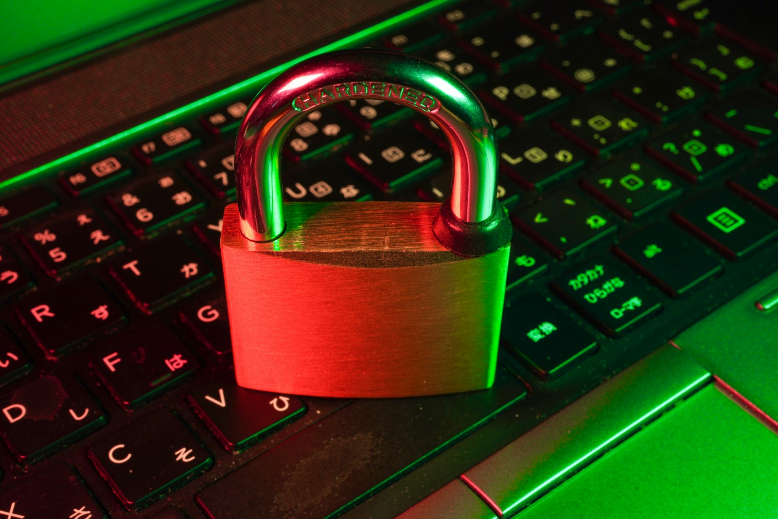 A brass padlock resting on a computer keyboard, lit from the sides by red and green light